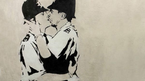 This undated photo provided by Keszler Gallery in New York, Tuesday, Feb. 18, 2014, shows "Kissing Coppers," a black-and-white stencil of two uniformed English "bobbies" (police officers) in a passionate clinch. The image was spray-painted in 2005 on the Prince Albert Pub in Brighton, England. Three works by the elusive British street artist Banksy, including two that had to be removed from the sides of buildings, are expected to bring hundreds of thousands of dollars Tuesday night at the Fine Art Auctions Miami. (AP Photo/ Keszler Gallery)